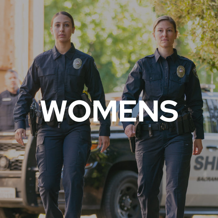 Two women in dark navy police uniforms walking outdoors in front of a vehicle, with the word 'WOMENS' overlaid across the center.