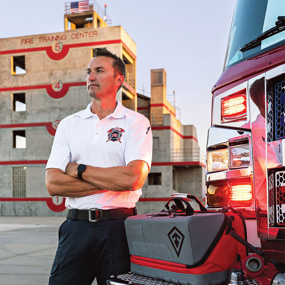 Image of man wearing white cotton polo standing near a fire truck